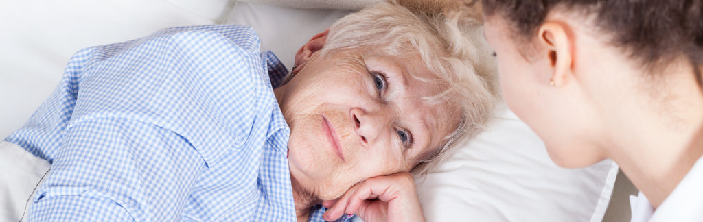 Image of elderly woman in bed talking to caregiver